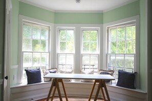 Una habitación con un rincón ventana con asientos, una mesa y vistas a árboles.