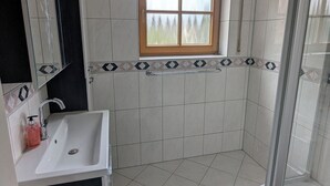 Une salle de bain avec un lavabo blanc, un miroir, une fenêtre et un espace douche.
