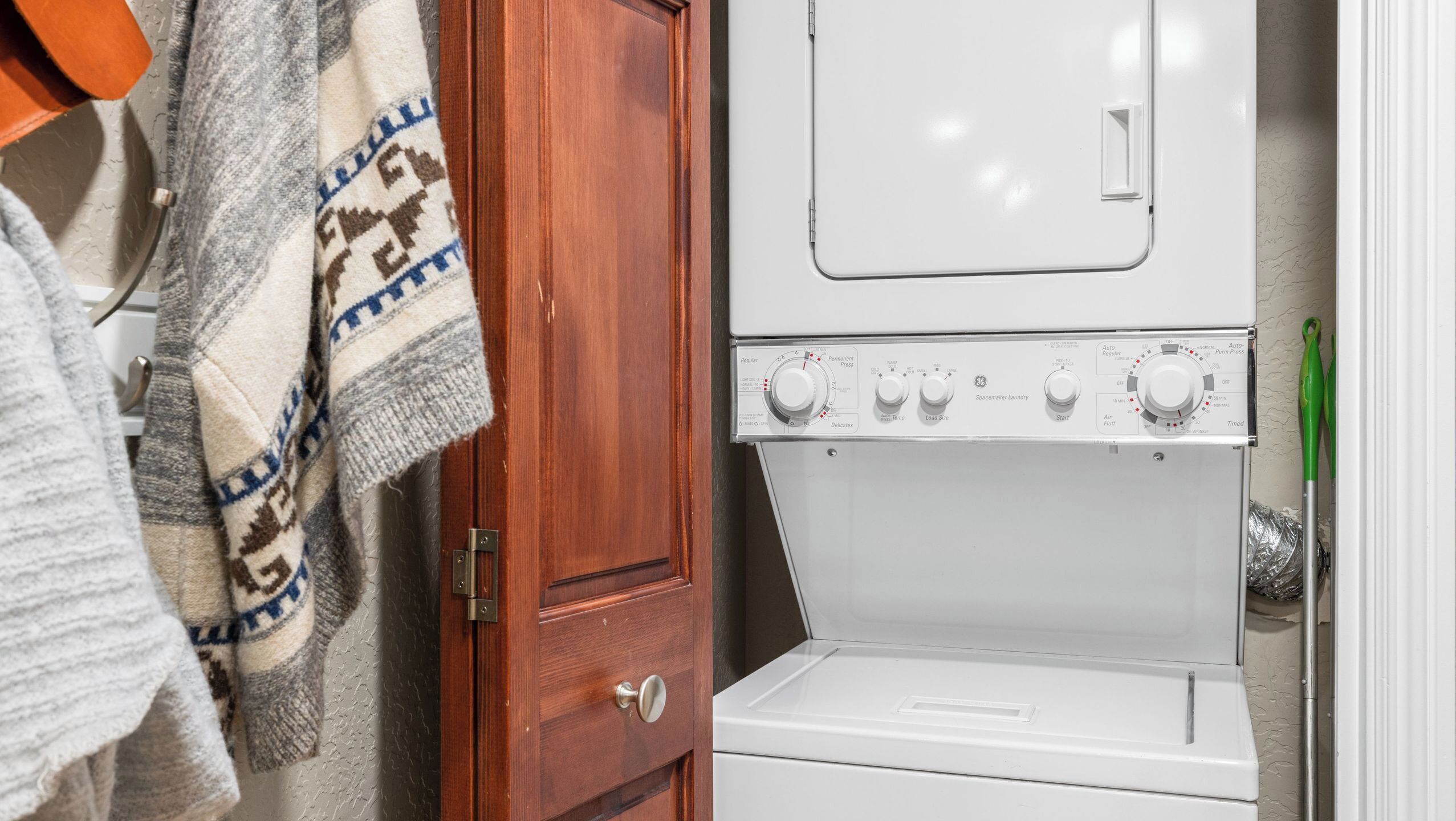 Une buanderie équipée d’un lave-linge et d’un sèche-linge superposés, d’une porte en bois et d’un porte-serviettes.