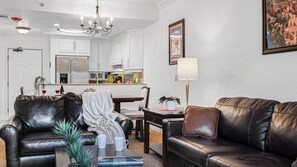 A living room with leather sofas, a coffee table with books and a plant, a dining area with a table and chairs, and a kitchen with white cabinets and stainless steel appliances. - Canyon Lodge at Westgate by Avantstay Park City Mountain Condo With Private Hot Tub + Views + Resort Amenities (Park City)