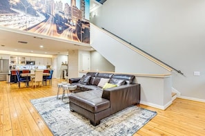 Ein geräumiger Wohnbereich mit moderner Küche im Hintergrund, einem Ledersofa und einer Treppe.