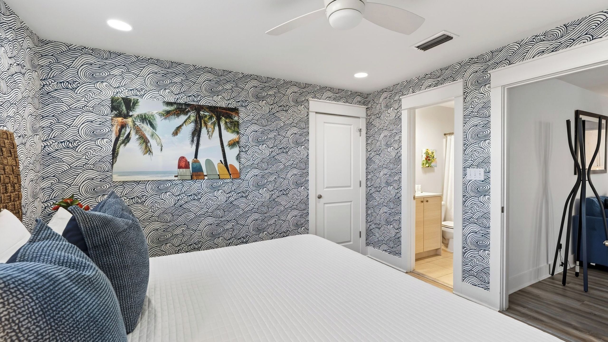 Une chambre avec un papier peint à motifs, un lit, un ventilateur de plafond et une vue sur la salle de bain.