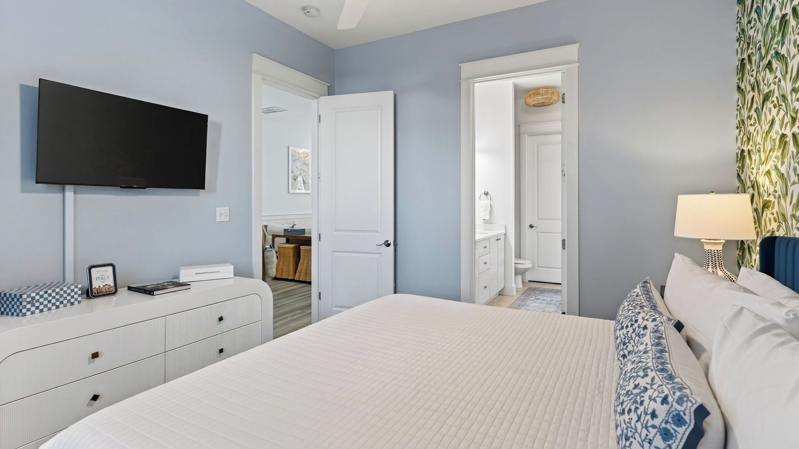 A bedroom with a bed, a TV, a dresser, and a bathroom visible through an open door.