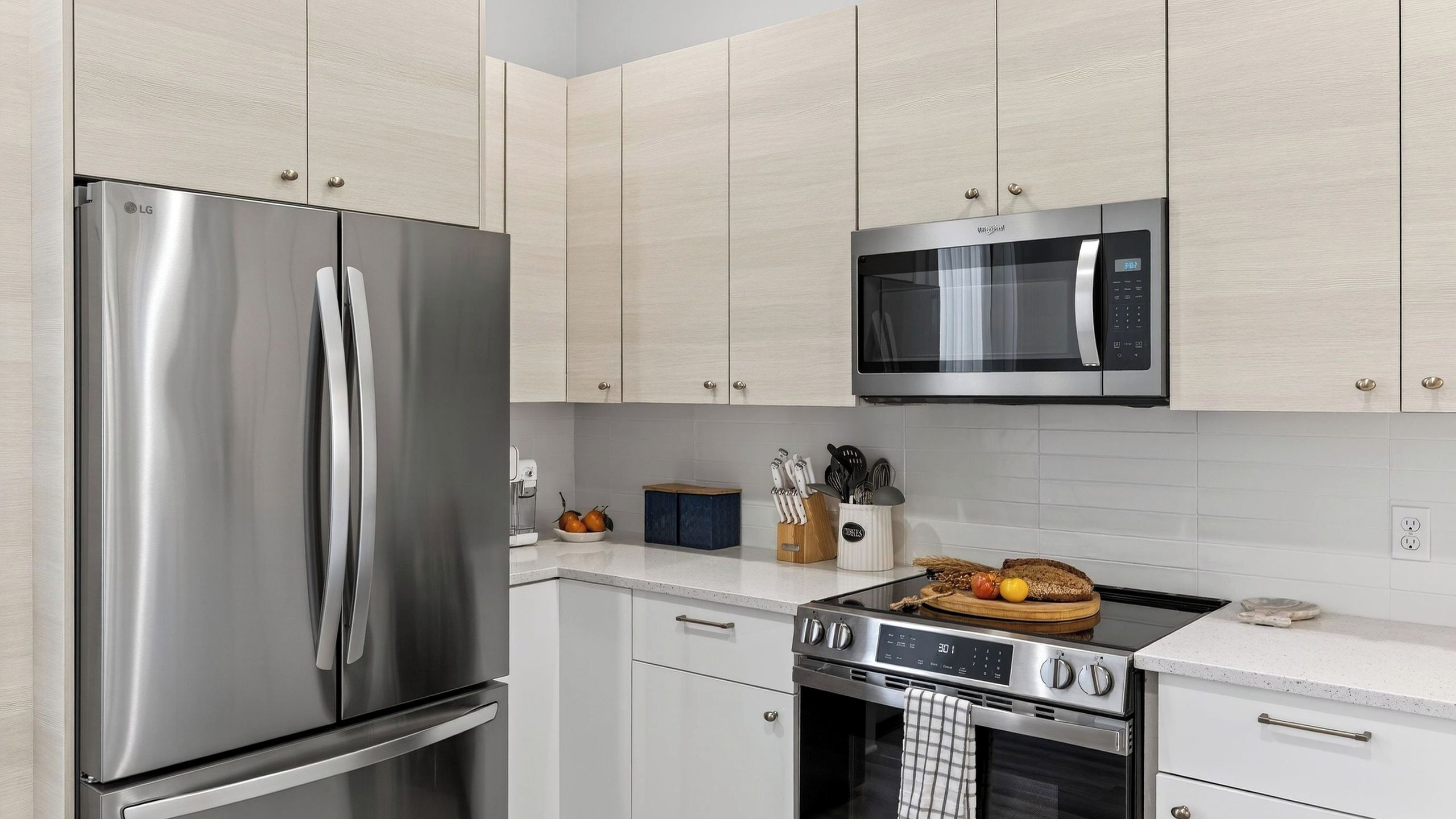 Een moderne keuken met roestvrijstalen apparatuur, licht houten kastjes en een wit aanrecht.