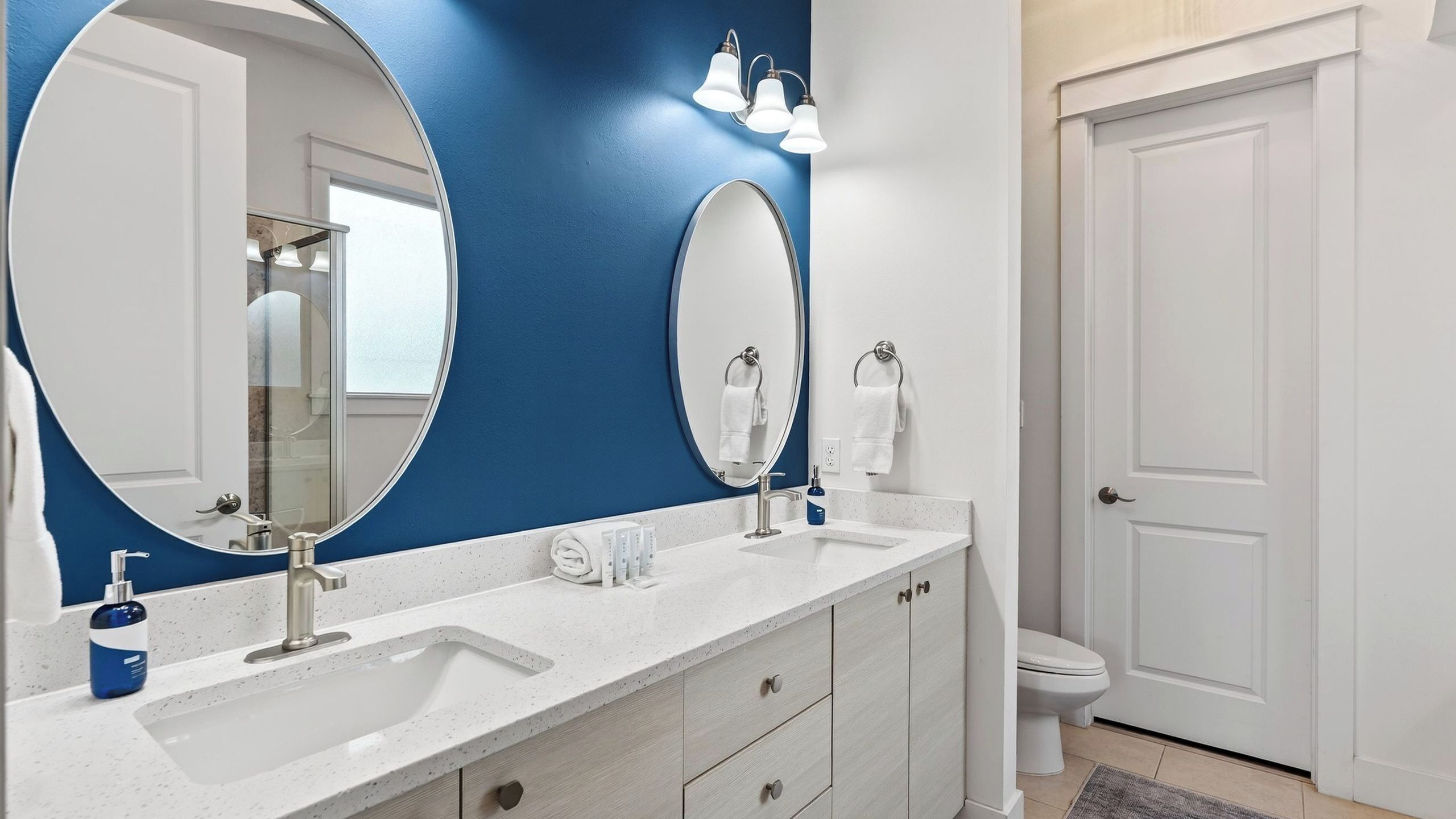 A bathroom with a large oval mirror, a white sink, a towel rack, and a toilet.