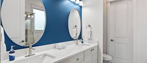 A bathroom with a large oval mirror, a white sink, a towel rack, and a toilet.