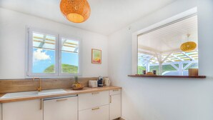 Een keuken met een houten aanrecht, witte kastjes, een dubbele spoelbak en een raam met uitzicht op groen.