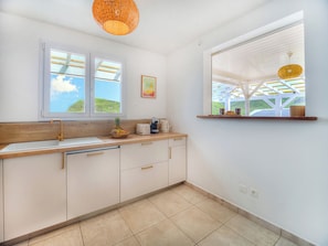 A kitchen with a wooden countertop, white cabinets, a double sink, and a window with a view of greenery.