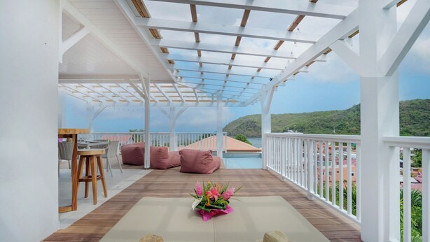 A covered outdoor seating area with wooden flooring, white railings, and a view of a mountainous landscape.