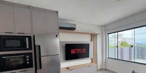 Une cuisine moderne équipée d’un four à micro-ondes, d’un four et d’un réfrigérateur encastrés. Un téléviseur à écran plat fixé au mur affiche le logo de Netflix.