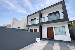 A modern two-story house with a balcony, large windows, and a grey exterior wall. - Sampaio's House - Gov. Celso Ramos - SC (Governador Celso Ramos)