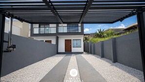 A modern two-story house with a covered driveway and a gravel pathway. - Sampaio's House - Gov. Celso Ramos - SC (Governador Celso Ramos)