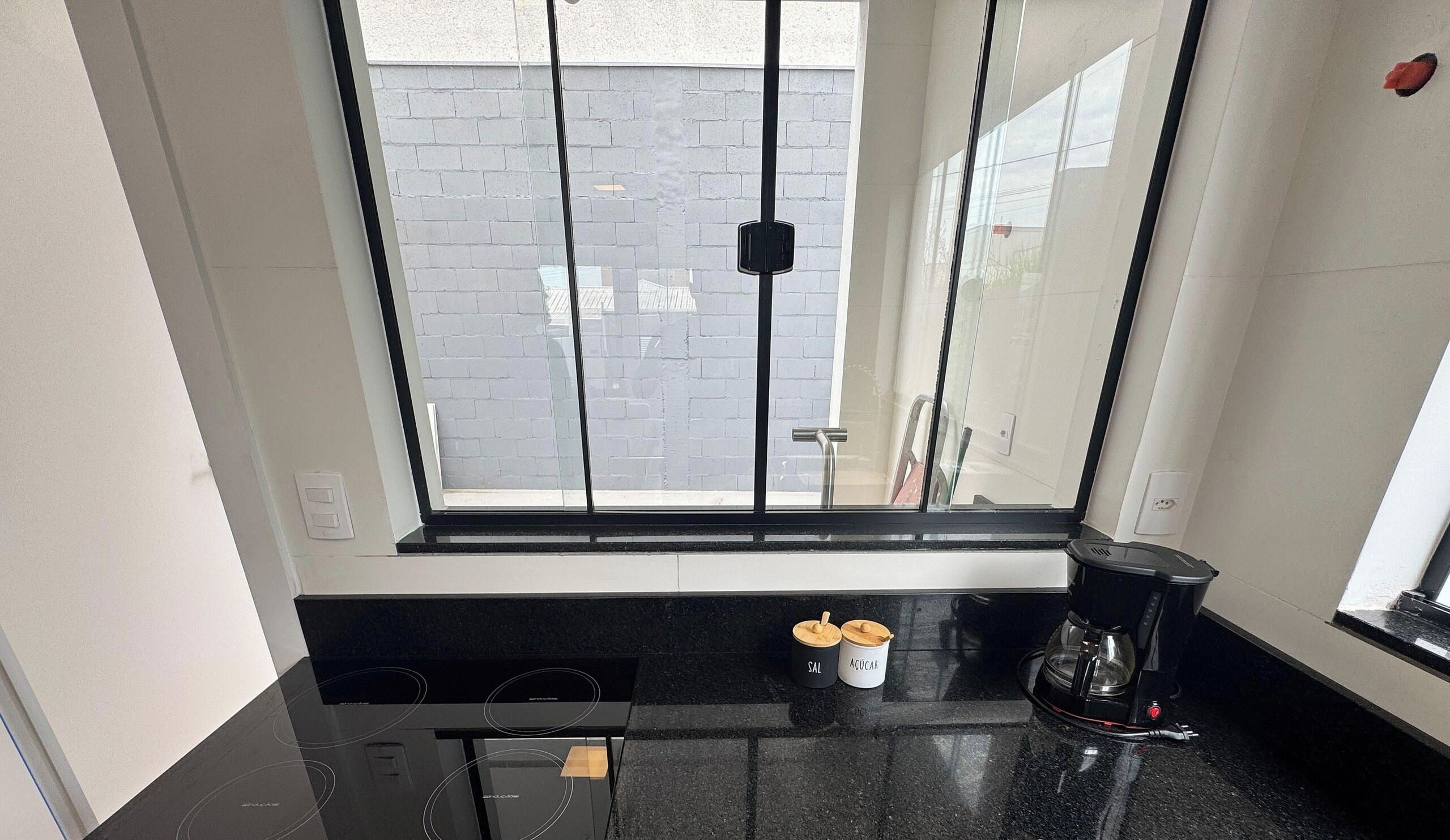 Cozinha com bancada preta, cafeteira e dois recipientes identificados com 'SAL' e 'AÇÚCAR'.