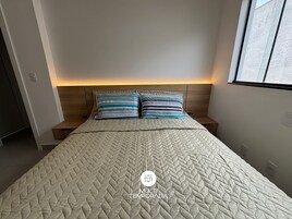 Un dormitorio con una cama, dos almohadas, una mesita de noche y un velador.