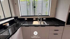 Moderni keittiö, jossa on musta työtaso, ruostumattomasta teräksestä valmistettu pesuallas ja ikkuna, josta avautuu näkymä puutarhaan.