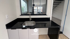 A kitchen with a black countertop, a window, and a view of a staircase. - Sampaio's House - Gov. Celso Ramos - SC (Governador Celso Ramos)