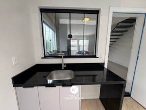 Une cuisine avec un plan de travail noir, une fenêtre et une vue sur un escalier.