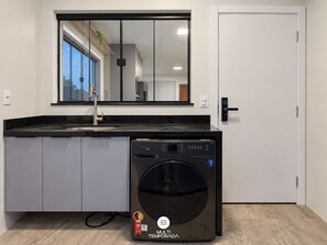 Une cuisine compacte équipée d’un lave-linge intégré, d’un grand miroir au-dessus de l’évier et d’une porte dotée d’une serrure moderne.