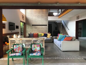 A spacious living area with a sofa set, a coffee table, and two green chairs with floral cushions. A staircase is visible in the background leading to an upper level. - Casa do Sol on Domingas Dias Beach in Ubatuba—250 m from the beach (Ubatuba)