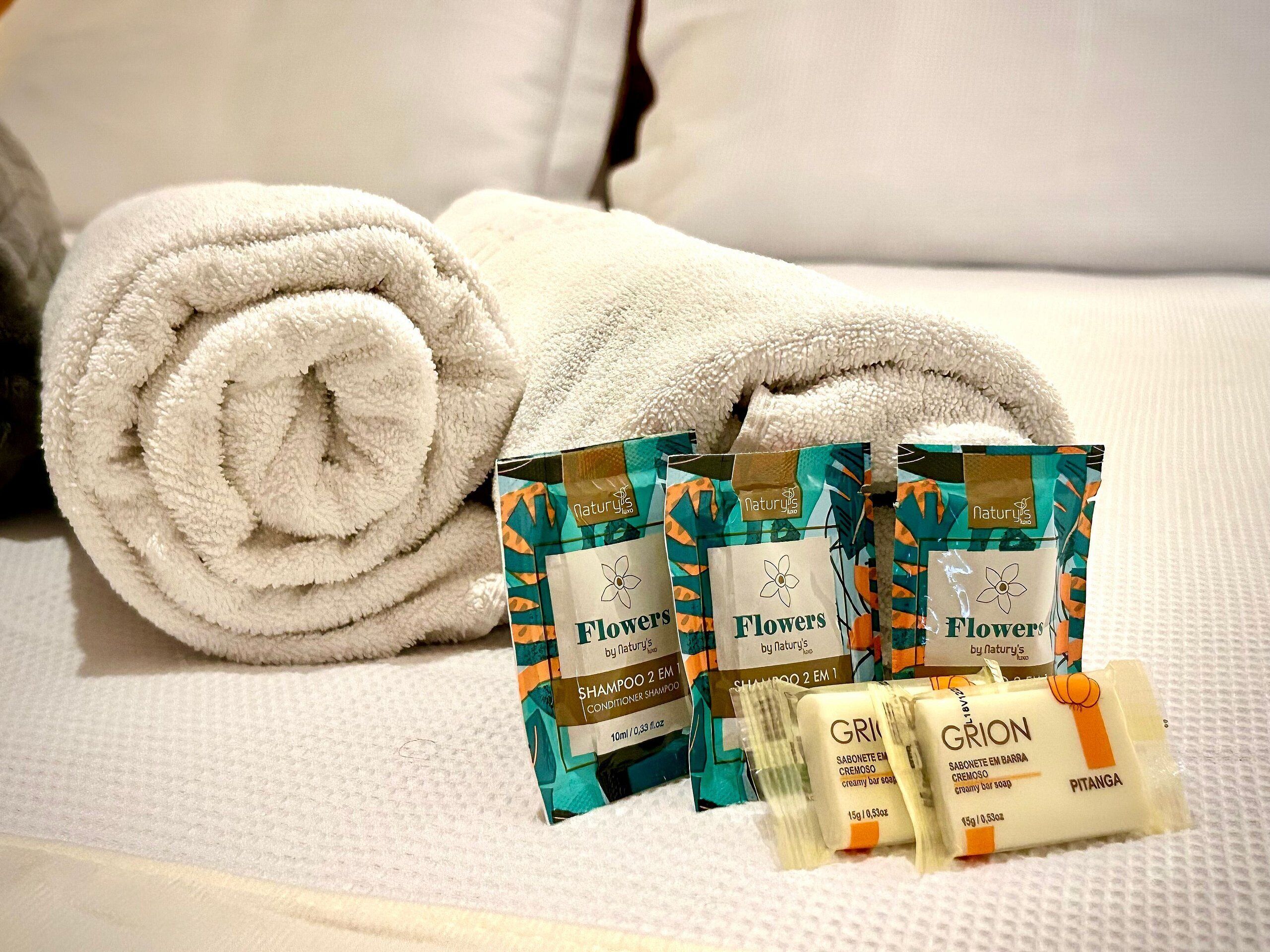 A neatly folded white towel, a set of toiletries including shampoo and conditioner, and a bar of soap on a textured surface.