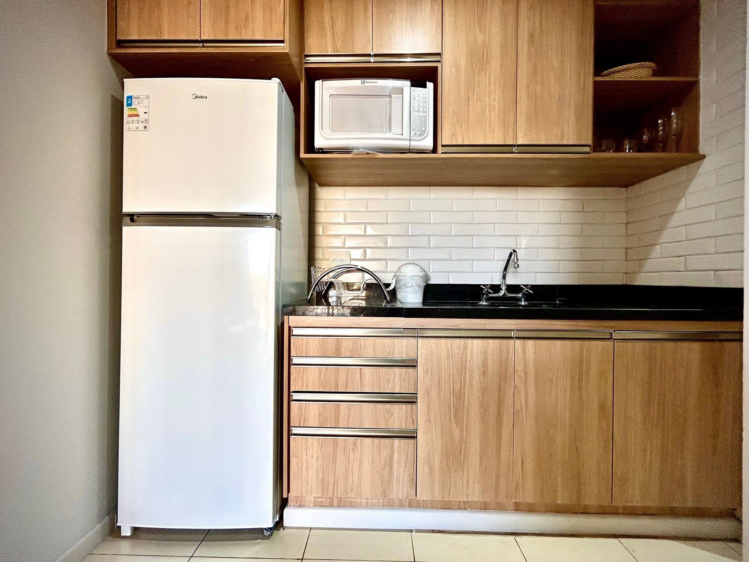 Una cocina con armarios de madera, un refrigerador blanco, un microondas y una encimera negra.