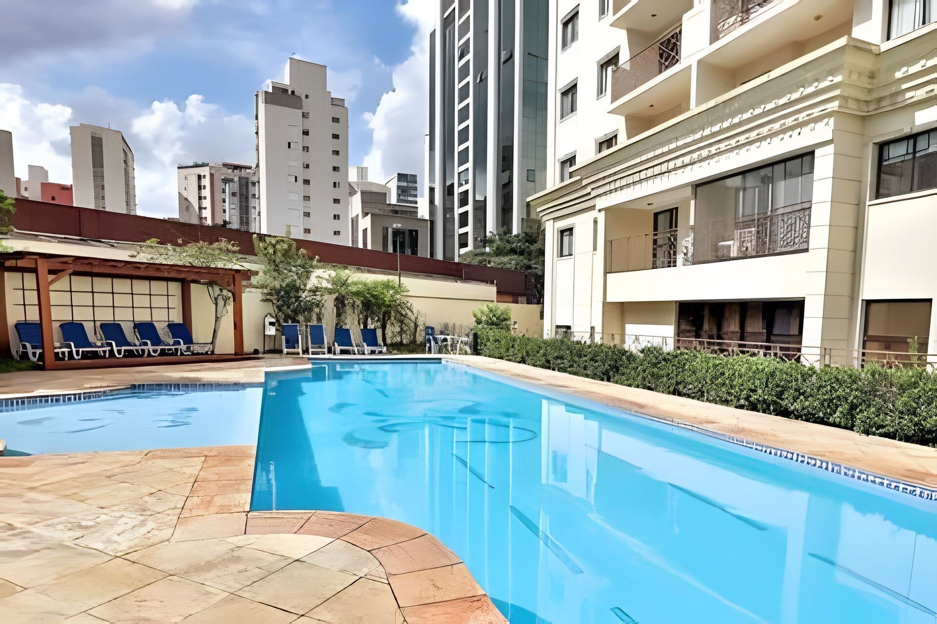 A swimming pool with lounge chairs, surrounded by a courtyard with buildings in the background.