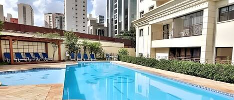 A swimming pool with lounge chairs, surrounded by a courtyard with buildings in the background.