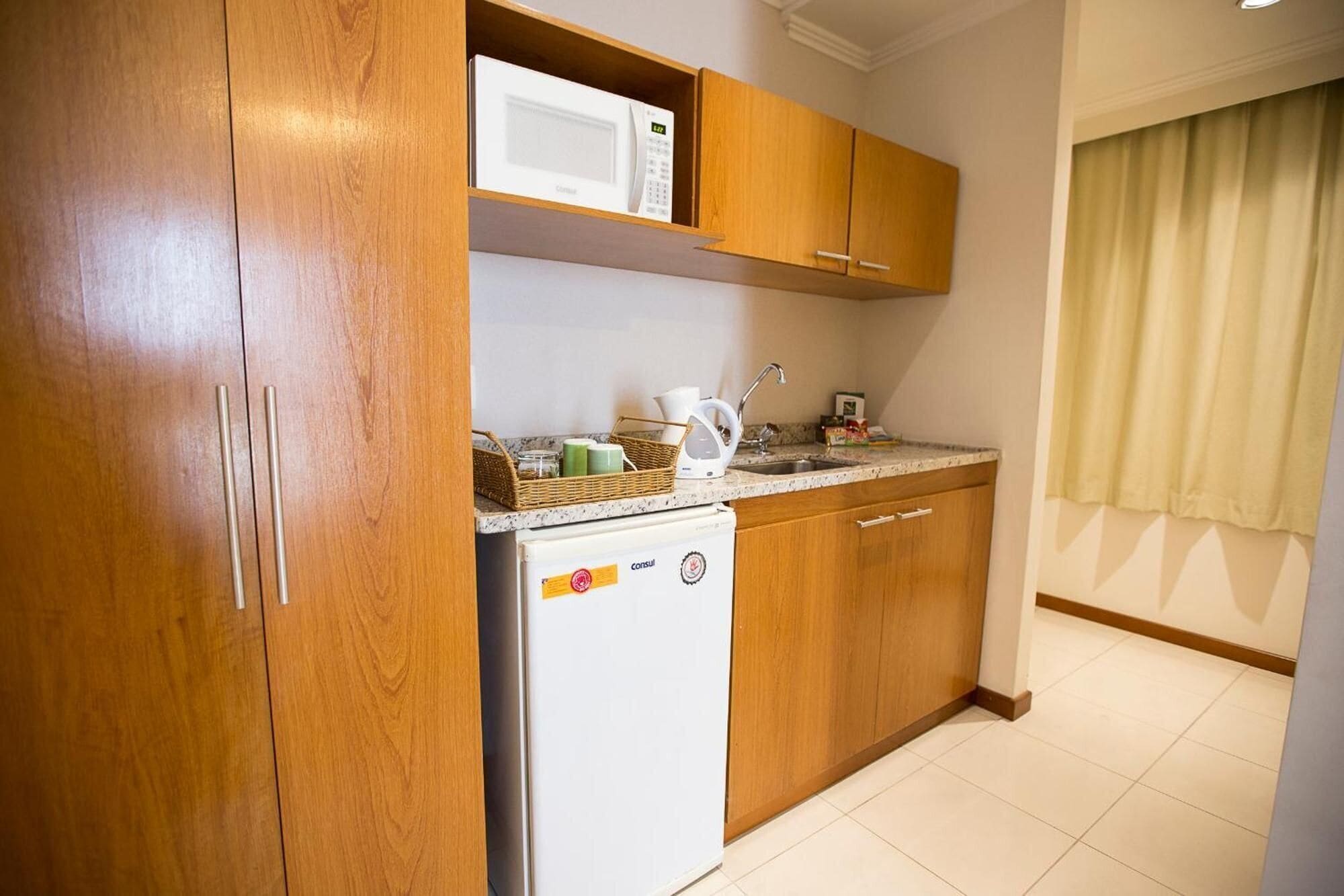 A compact kitchen with wooden cabinets, a white refrigerator, a microwave, and a kettle on the countertop.