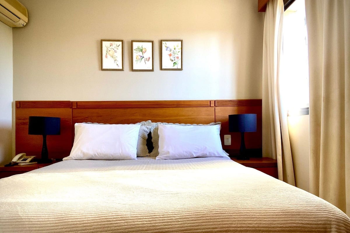 Una habitación de hotel con una cama grande, dos lámparas de noche, un teléfono y tres cuadros con flores en la pared.