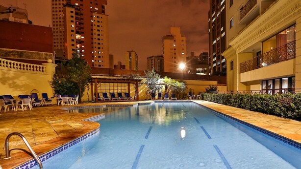 An indoor swimming pool with clear blue water, surrounded by lounge chairs and a tiled deck. - World Class Stay - Vila Olímpia (São Paulo)
