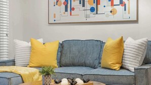 A living room with a blue sofa, yellow pillows, a round wooden coffee table, and a geometric abstract painting on the wall. - 2 Bed Midtown Loft Midtown (Atlanta)