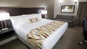 Una habitación de hotel con una cama grande, dos lámparas de noche, un escritorio con teléfono, una silla y un sofá.