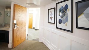 Un couloir orné de tableaux encadrés, une porte en bois et un mur blanc avec des panneaux décoratifs.