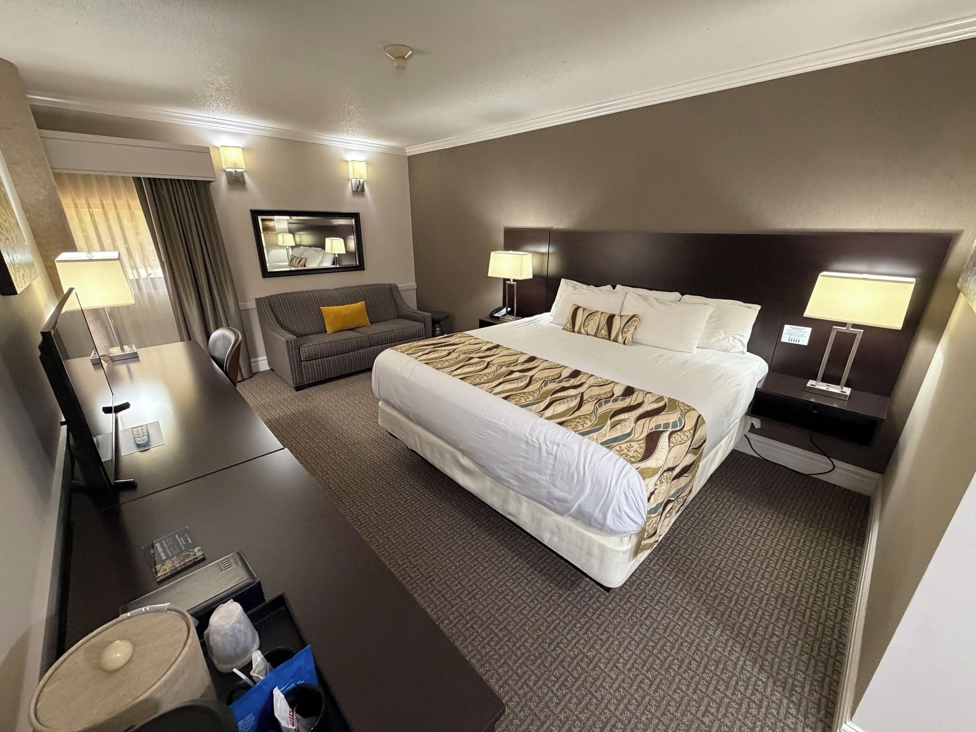 A hotel room with a large bed, a sofa, a desk, and a mirror.
