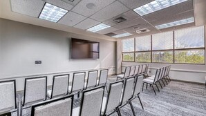 A conference room with rows of chairs, a flat-screen TV mounted on the wall, and large windows with blinds. - University Inn (Logan)