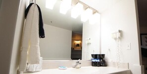 A bathroom with a white sink, a mirror, a towel rack with a white towel, a coffee maker, and a telephone. - University Inn (Logan)