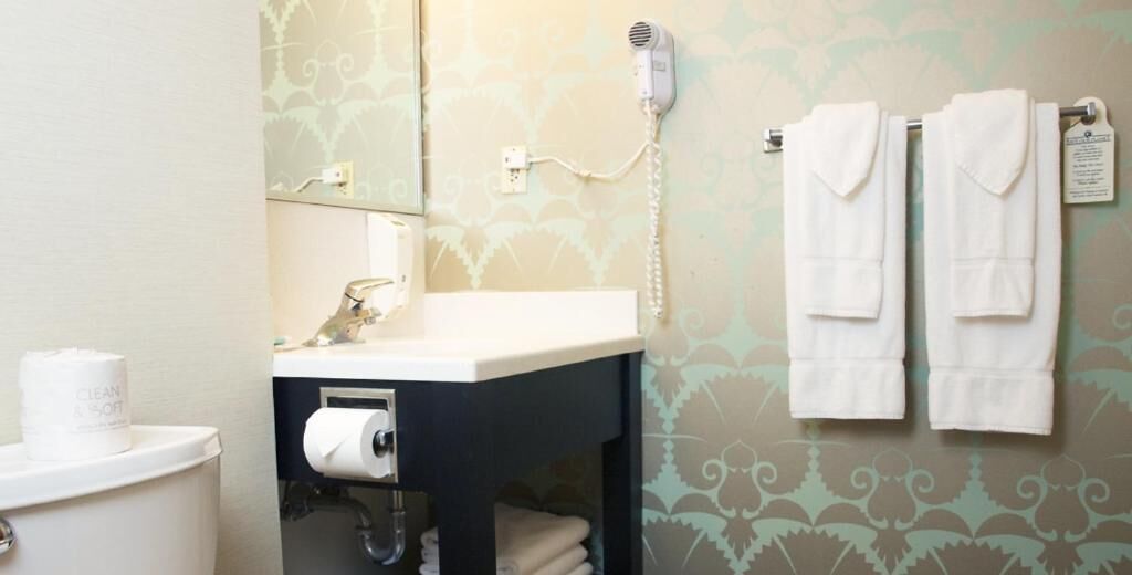 Un baño con lavamanos, inodoro y un secador de pelo fijado a la pared.