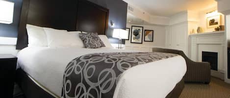Une chambre d’hôtel avec un grand lit, une table de chevet, une chaise, une cheminée et des œuvres d’art encadrées accrochées au mur.