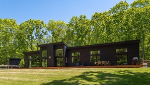 Un edifici modern de dos pisos amb finestres grans, una terrassa i un jardí amb gespa.