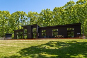 Un bâtiment moderne à deux étages, doté de grandes fenêtres, d’une terrasse et d’une cour gazonnée.