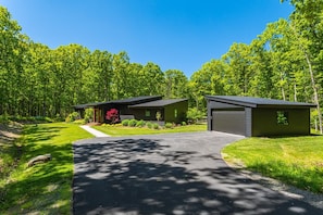 A two-story building with a driveway leading to a garage, surrounded by lush greenery and trees.