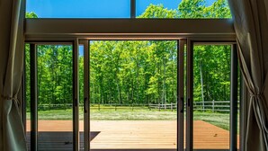 Habitació amb grans portes corredisses de vidre que donen a una terrassa exterior amb sòl de fusta i vista a una zona boscosa.