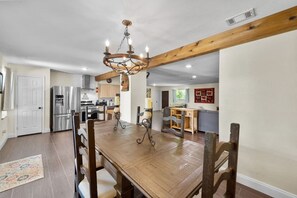 Un comedor amplio con una mesa y sillas de madera, un candelabro y una cocina al fondo.