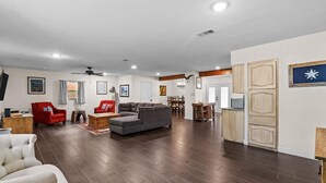 A spacious living area with a grey sofa, red armchair, and a white armchair. There is a wooden coffee table and a dining table with chairs. The room has wooden flooring and white walls. - Bexar Charming 3-bedroom MidTerm (Arlington)