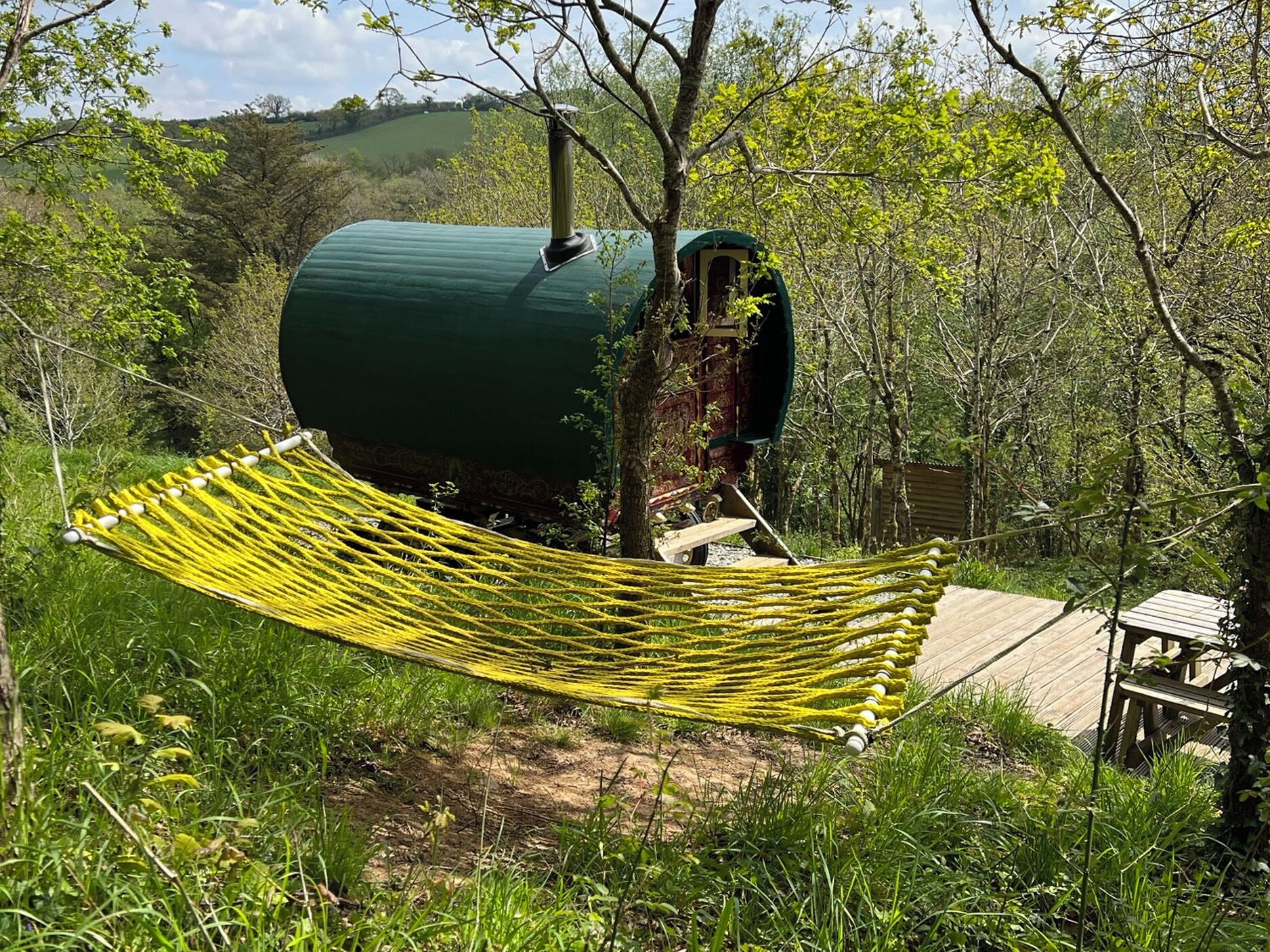 A hammock tied between trees, a green structure resembling a water tank, and a wooden deck.