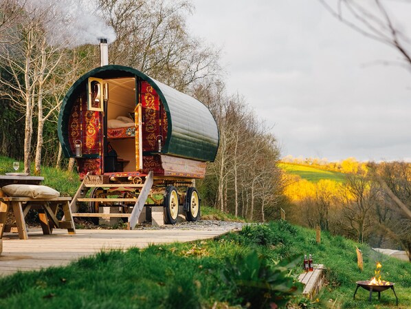 Une caravane immobile, dotée d’une entrée ouverte, d’une terrasse en bois et d’un foyer.