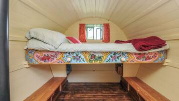 A small, cozy attic bedroom with a single bed, wooden benches, and a window with curtains.