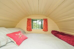A room with a sloped ceiling, a window with curtains, a bed with pillows, and a red blanket. - Goldfinch (Launceston)