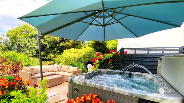 A hot tub surrounded by outdoor furniture and vibrant flowers. - Muntham Luxury Town House With Hot Tub (Torquay)