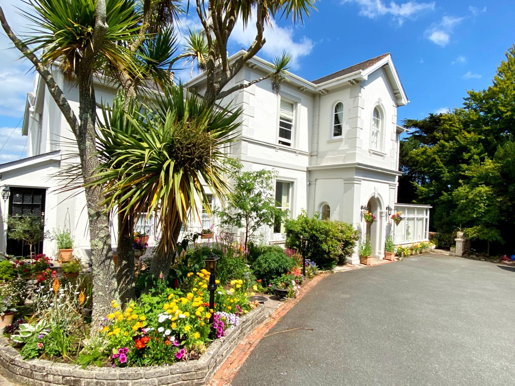 A large white building with a symmetrical facade, multiple windows, and a well-maintained garden with various plants and flowers.